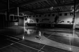 grayscale photo of boy holding ball standing on basketball court